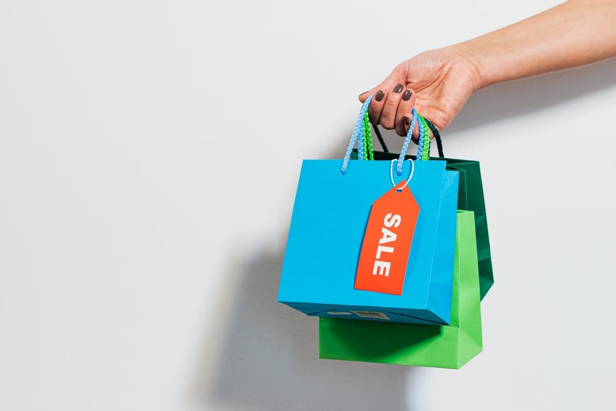 Mão segurando pequenas sacolas de compras coloridas com uma etiqueta de promoção