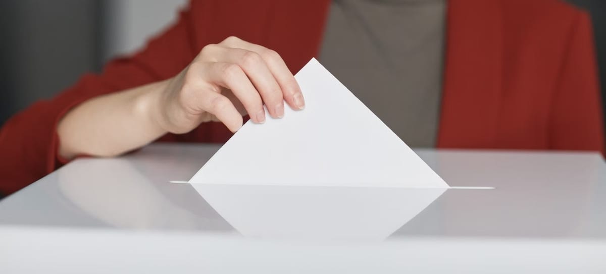Mão colocando um envelope branco em uma urna de votação