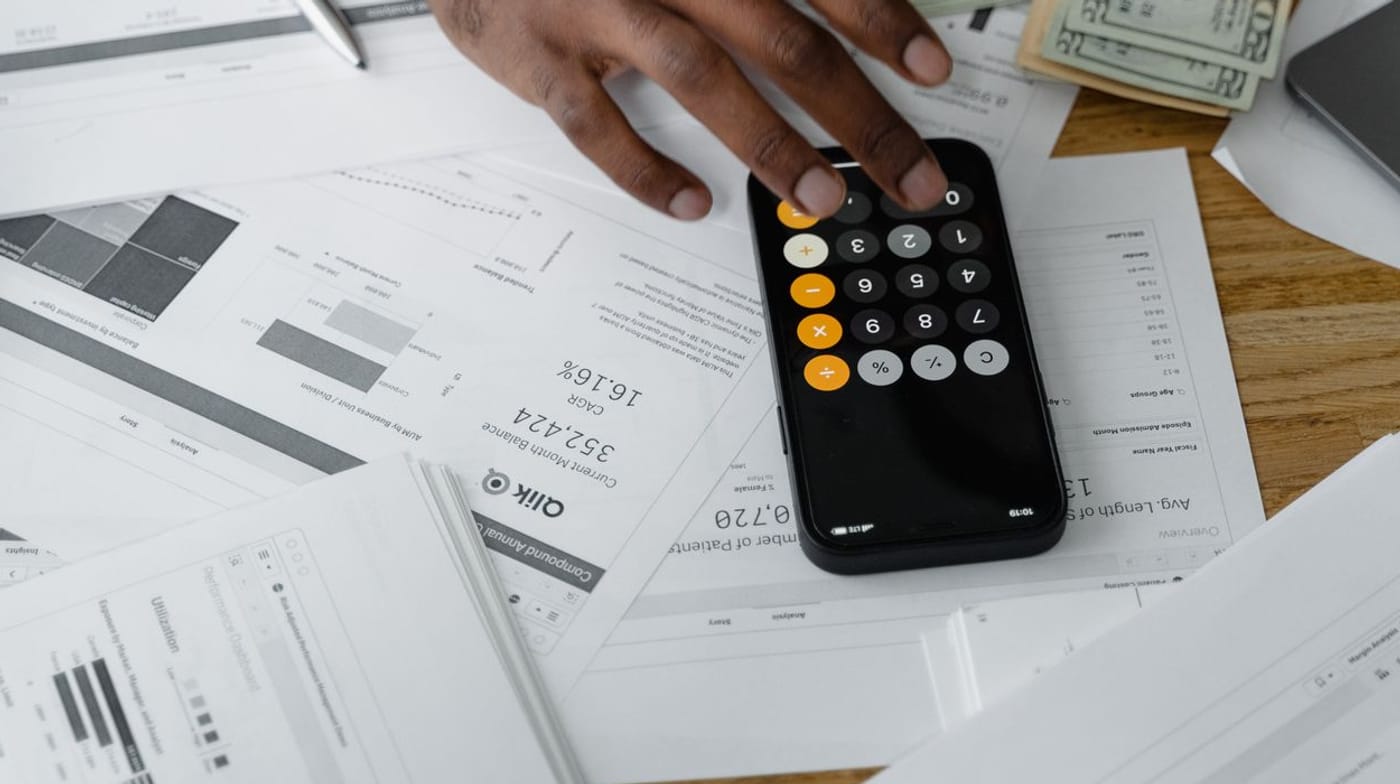 Mão usando a calculadora do celular sobre relatórios e papéis financeiros