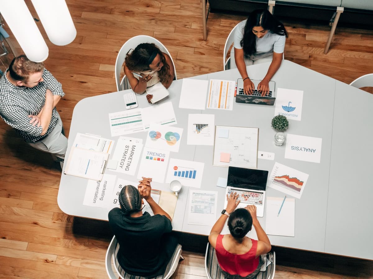 Equipe em reunião ao redor de uma mesa com gráficos, relatórios e notebooks